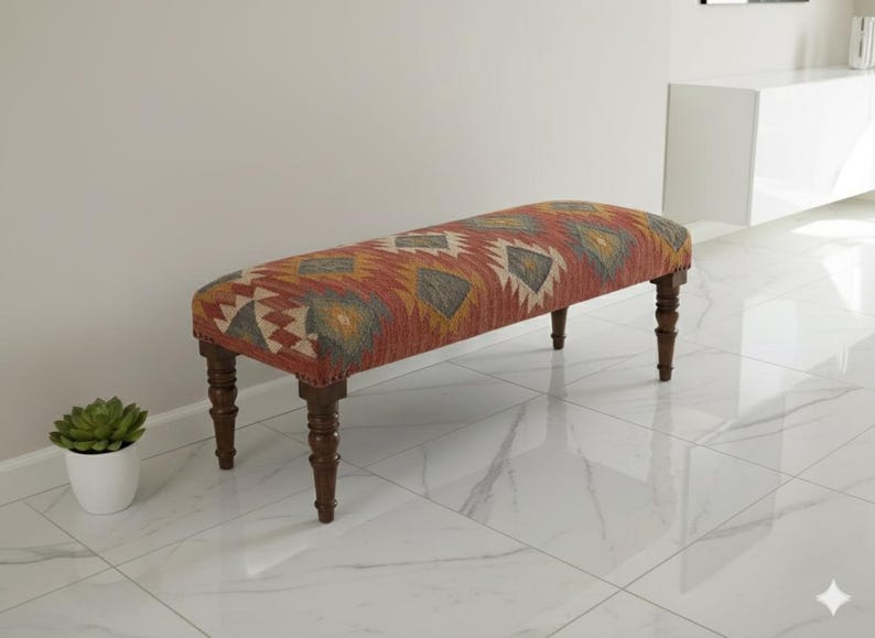 May include: Upholstered bench with a patterned design in red, yellow, and cream colors. The bench has dark brown wooden legs. The bench is a decorative furniture piece.