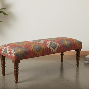 May include: A long, upholstered bench with a patterned fabric in shades of red, yellow, and gray. The bench has dark wooden legs and a rounded top, suitable for a living room or entryway.
