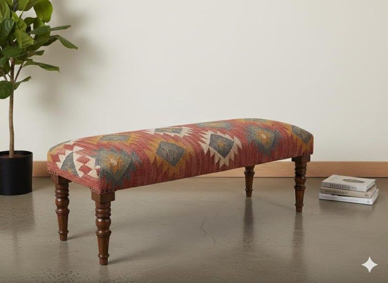 May include: A long, upholstered bench with a patterned fabric in shades of red, yellow, and gray. The bench has dark wooden legs and a rounded top, suitable for a living room or entryway.