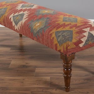 May include: A long, upholstered bench with a patterned top in shades of red, yellow, gray, and white. The bench has turned wooden legs and is suitable for a living room or entryway. The bench measures approximately 48 inches long.