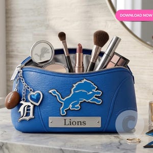 May include: A blue cosmetic bag with a Detroit Lions logo and a football charm. The bag is filled with makeup brushes, lipstick, and compacts. The bag is on a marble surface.