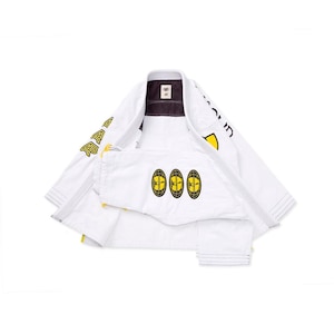 May include: A white martial arts gi featuring yellow and black graphic patches on the chest and sleeves. The jacket displays three oval logos with globe designs and text, along with bold lettering on the sleeves and collar area.