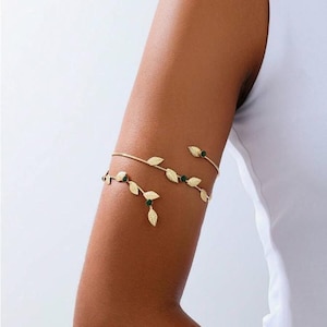 May include: Gold-coloured arm cuff with a delicate leaf design and small green accents. The jewellery is worn on the upper arm and has an adjustable design. The arm cuff is a stylish accessory.