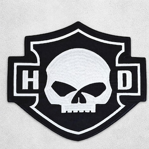 May include: A black and white embroidered patch with a skull design. The patch is shield-shaped, with the letters "H" and "D" flanking the skull. The skull is white, set against a black background.