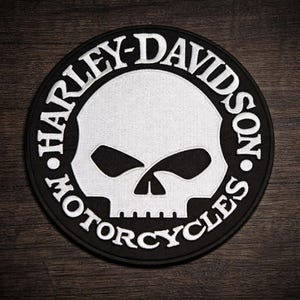 May include: A round, black and white Harley-Davidson Motorcycles patch. The patch features a white skull in the center, surrounded by the words "HARLEY-DAVIDSON MOTORCYCLES" in white lettering on a black background.