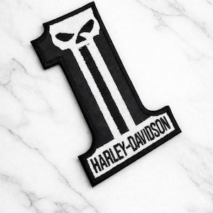 Op de afbeelding: Zwart-wit Harley-Davidson-patch in de vorm van het nummer één. De patch heeft een schedelontwerp aan de bovenkant en het Harley-Davidson-logo aan de onderkant. De patch is geborduurd.