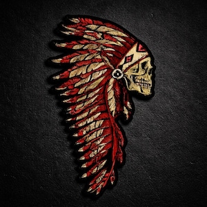 May include: Embroidered patch depicting a skull wearing a Native American headdress. The headdress is red and gold, with detailed feather patterns. The skull is a light tan colour, and the patch has a black border.