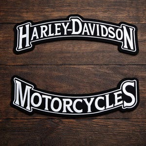 Peut inclure: Deux écussons Harley-Davidson noirs et blancs. Le patch supérieur indique "HARLEY-DAVIDSON" dans un design incurvé. Le patch inférieur indique "MOTORCYCLES" dans un style similaire. Les deux écussons ont un fond noir et des lettres blanches.