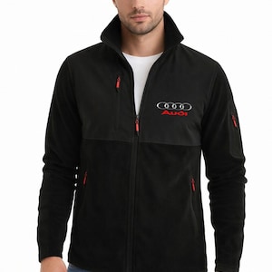 May include: Black fleece jacket with a high collar and red zipper accents. The Audi logo is embroidered in red and silver on the chest. The jacket has a full-length zipper and two side pockets.