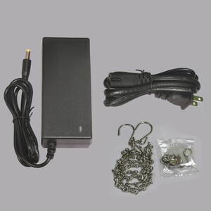 May include: A black power adapter with a DC connector, a black power cord, a silver chain, and a small bag of hardware. The power adapter is rectangular and has a label on the side.