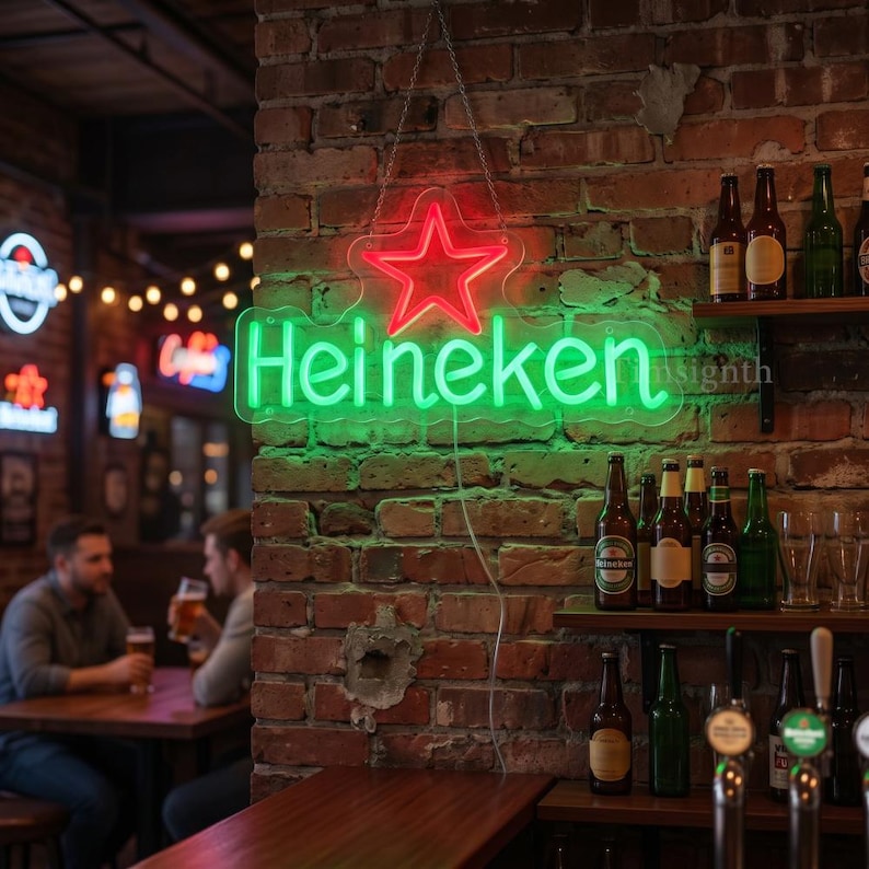 May include: A neon sign for Heineken beer hangs on a brick wall. The sign has a red star and green lettering. The bar scene includes bottles of beer on shelves and two people sitting at a table.