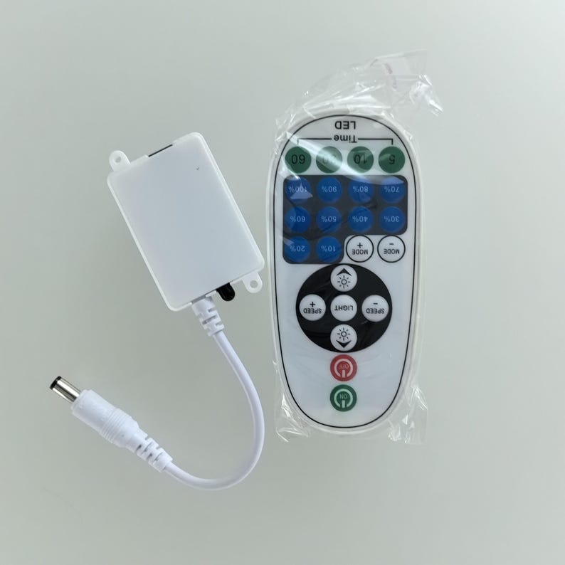 May include: A white LED light controller with a remote control. The remote has buttons for speed, light, mode, and power, along with percentage settings. The controller has a power cable and a DC connector.