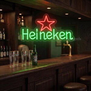 May include: A neon sign with the word "Heineken" in green, topped with a red star, hangs above a bar. A green Heineken bottle and several glasses sit on the wooden bar. The bar has a classic, dark wood design.