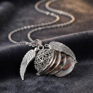 May include: A silver-toned locket necklace featuring a spherical cage pendant with an intricate star pattern and two attached wings. The locket opens to reveal multiple circular photo frames arranged in a stack, suspended from a delicate metal chain.