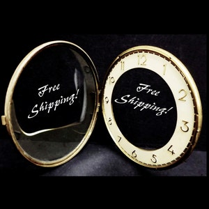 May include: A gold-colored compact mirror with a white face and black numbers. The mirror is open and the inside of the mirror says "Free Shipping!" in white cursive writing.