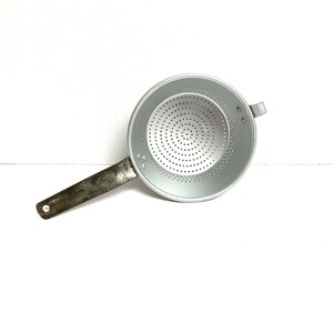 May include: A silver metal strainer with a long handle. The strainer has a circular shape with a series of small holes.