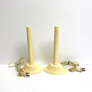 May include: Two ivory-colored electric candle lamps with cords and plugs. The candles have a dripping wax design.