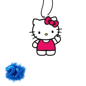 Könnte beinhalten: Ein weißer Hello Kitty-Lufterfrischer mit rosa Kleid und Schleife. Die Cartoonfigur hat schwarze Schnurrhaare, Augen und eine kleine gelbe Nase. Oben ist eine schwarze Schnur zum Aufhängen befestigt.