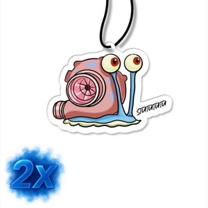 Könnte beinhalten: Ein Cartoon-Lufterfrischer in Form einer Schnecke, die als Turbolader gestaltet ist. Die Schnecke ist rosa und blau mit großen Kulleraugen und einer schwarzen Schnur zum Aufhängen. Der Text "2X" befindet sich in der unteren linken Ecke.