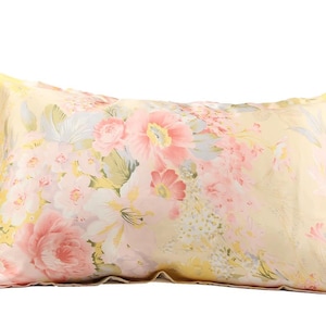 May include: A rectangular pillow with a floral pattern. The pillow features a light yellow background with pink, white, and yellow flowers. The pillow is designed for decorative or sleeping purposes.