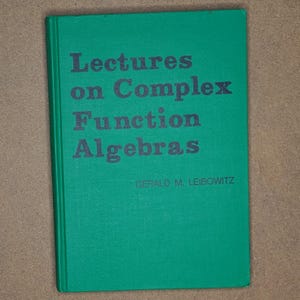 May include: A hardcover book with a green cover. The title "Lectures on Complex Function Algebras" is printed in dark gray letters. The author's name, Gerald M. Leibowitz, is printed below the title. The book is on a brown surface.