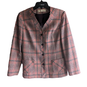 May include: A vintage blazer in a red, black, and white plaid pattern. The jacket has a V-neck, three buttons, and two front pockets. The blazer is hanging on a black hanger.
