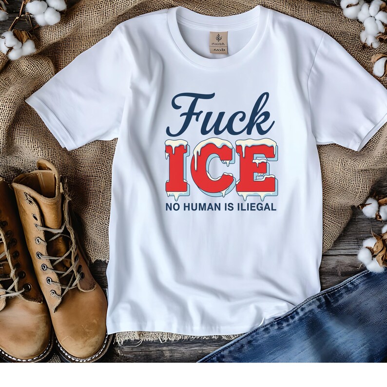 May include: White t-shirt with the text "Fuck ICE" in blue and red, with the words "NO HUMAN IS ILIEGAL" below. The shirt is displayed on a burlap surface with brown boots and blue jeans.