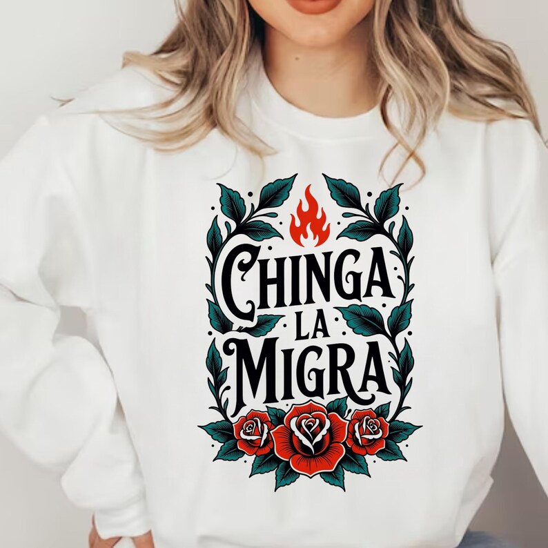 May include: White sweatshirt featuring the text "Chinga La Migra" in black script, framed by green leaves and red roses. A red flame sits above the text. The design is centered on the front of the sweatshirt.