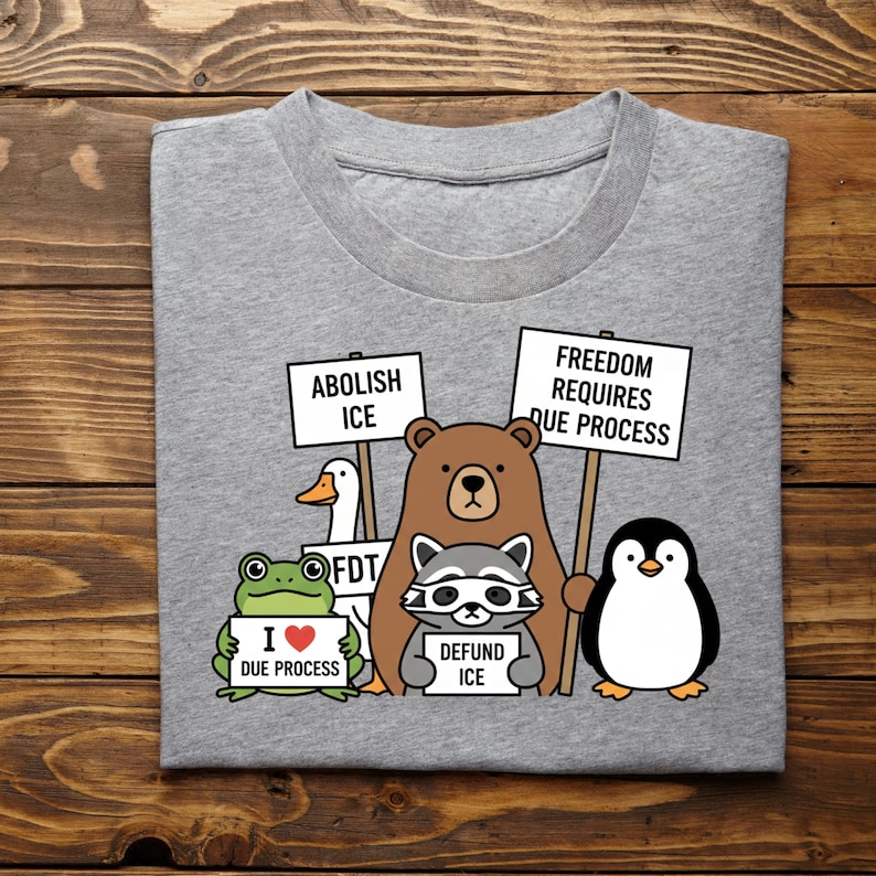 May include: A heather gray t-shirt featuring a graphic of cartoon animals protesting with signs. The signs read "Abolish ICE", "Freedom Requires Due Process", and "Defund ICE". A frog holds a sign that says "I ❤️ Due Process".