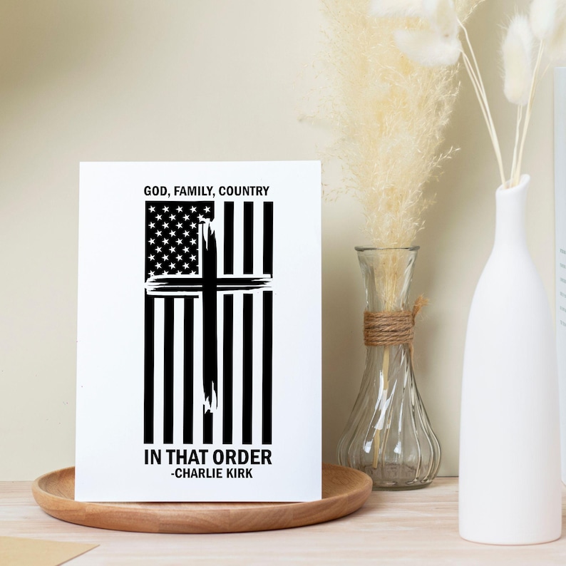 May include: A white rectangular print with a black and white design. The design features a cross over an American flag. The text at the top reads "GOD, FAMILY, COUNTRY" and the text at the bottom reads "IN THAT ORDER -CHARLIE KIRK".