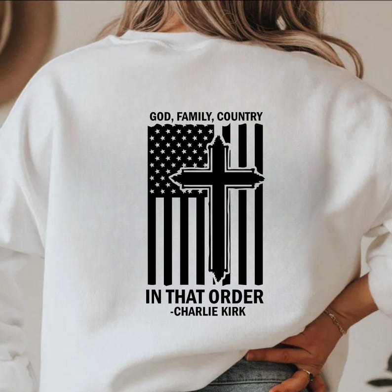 May include: White sweatshirt featuring a black and white graphic of an American flag and a cross. The text "GOD, FAMILY, COUNTRY" is above the flag, and "IN THAT ORDER -CHARLIE KIRK" is below.