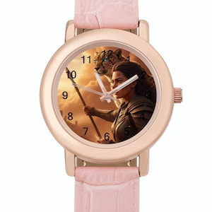 May include: A rose gold wristwatch with a pale pink leather strap. The watch face depicts a woman with a spear and a leopard against a sunset. The watch has a round face with black numerals. The strap is approximately 20 cm long.
