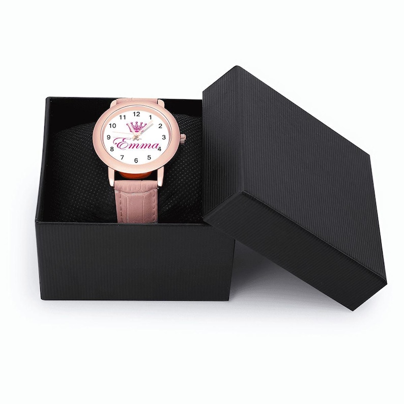 May include: A rose gold wristwatch with a pink leather band is displayed in an open black gift box. The watch face is white with black numerals and the name "Emma" in pink script, topped with a pink crown graphic.