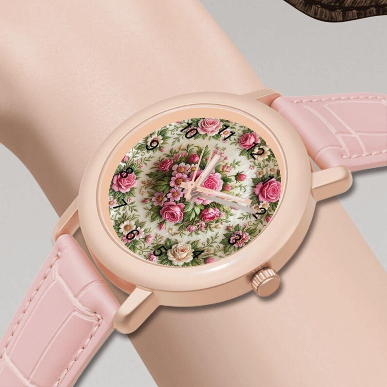 May include: A rose gold wristwatch with a light pink leather band. The watch face features a floral design with pink roses and green leaves. The watch is on a wrist.