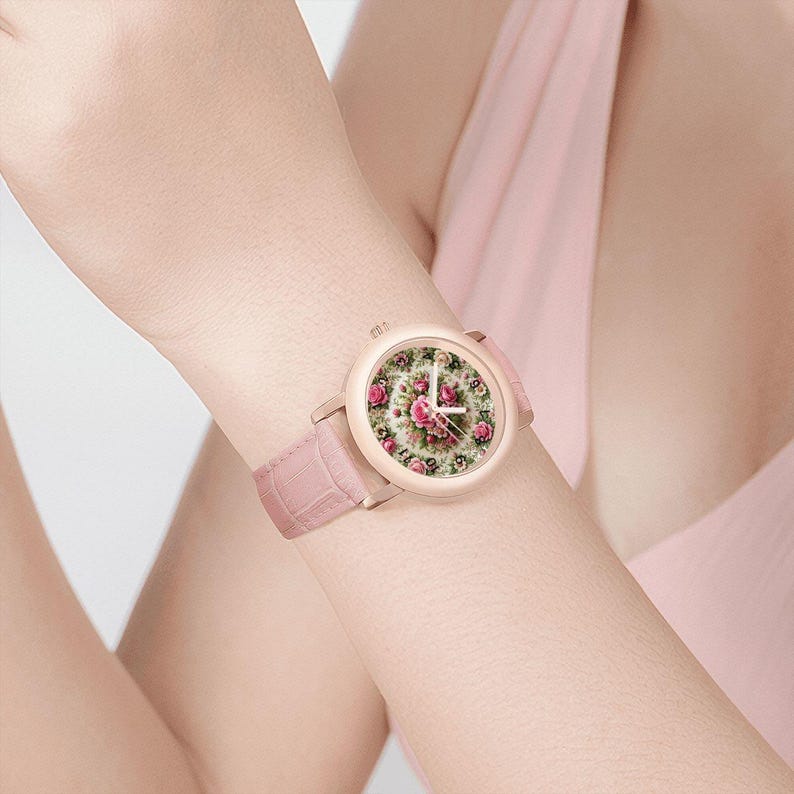 May include: A pink wristwatch with a floral design on the face. The watch has a light pink leather band and a gold-colored case. The watch face features a pattern of pink roses and green leaves.