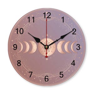 May include: A round wall clock with a celestial design. The clock face is a gradient of purple and rose gold, featuring a moon phase illustration and constellations. Black hands indicate the time. The clock measures approximately 12 inches in diameter.