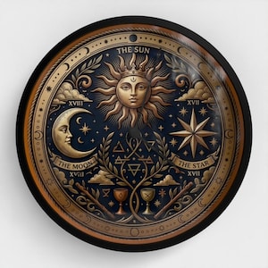 May include: A round wall clock with a dark blue face featuring gold celestial illustrations. The design includes a central sun, a crescent moon labeled THE MOON XVIII, a star labeled THE STAR XVII, and the text THE SUN. Two chalices and wands are depicted.