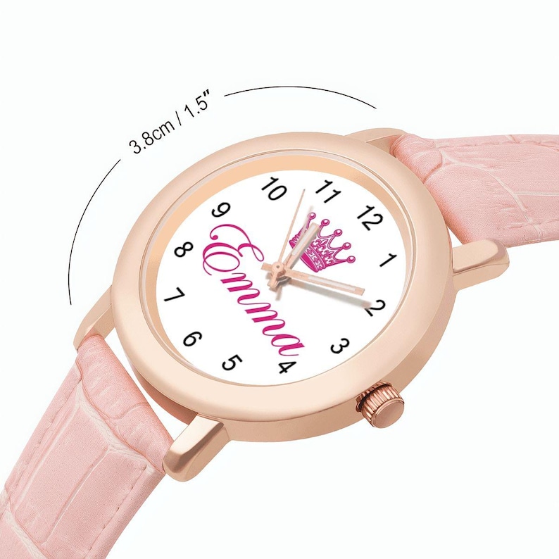 May include: A rose gold watch with a white face featuring the name "Emma" in pink script and a pink crown. The watch has a pink leather band and the face is 1.5 inches in diameter.