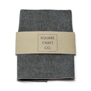 May include: A folded dark gray fabric square with a textured weave, wrapped in a tan paper band featuring the text "HANDMADE SQUARE CRAFT CO. POCKETWEAR" enclosed in a rectangular border. The fabric has a consistent charcoal tone.