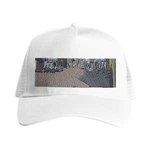 May include: White trucker hat with a mesh back and a curved brim. The front panel features an embroidered rectangular design with a cityscape in shades of gray, blue, and brown.