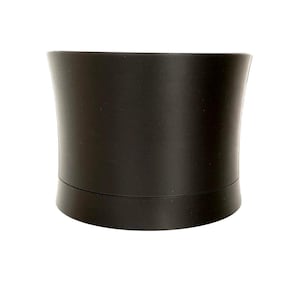 May include: A matte black cylindrical container with a slightly concave profile and a horizontal seam near the base. The object features a smooth, solid dark finish and a curved, symmetrical shape that tapers inward toward the center.
