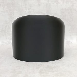 May include: A matte black cylindrical object with a smooth, solid surface and a rounded top edge. The item features a clean, uniform design with no visible markings, textures, or additional components, presenting a simple, geometric form.