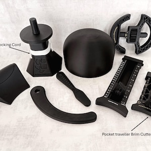 May include: A collection of black hat-making tools including a 1-meter blocking cord, a dome-shaped block, a curved handle, a flat curved piece, a circular frame, and a pocket traveller brim cutter with clearly marked inch and cm measurements.
