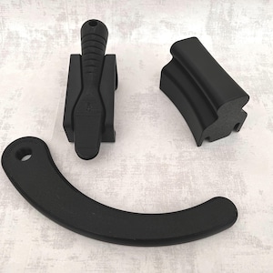 Op de afbeelding: Zwarte 3D-geprinte objecten, waaronder een handvat, een gebogen stuk met een gat en een gelaagde, gebogen component. De objecten zijn gerangschikt op een licht oppervlak, waarbij hun vormen en texturen worden benadrukt.