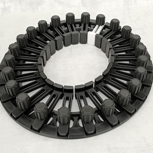 May include: A circular mechanical assembly featuring a series of black plastic radial arms, each topped with a textured cylindrical knob. The structure is arranged in a ring formation, with one distinct white plastic component integrated into the sequence.