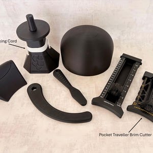 May include: An assortment of black hat-making tools, including a blocking cord, a curved shaping tool, a brim cutter, and a rounded hat form. The text "1 meter Blocking Cord" and "Pocket Traveller Brim Cutter" are visible.