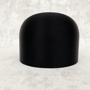 Könnte beinhalten: Ein schwarzes, kuppelförmiges Objekt mit glatter, matter Oberfläche und abgerundeter Oberseite. Es hat eine zylindrische Form und steht auf einer weißen Oberfläche. Es könnte ein dekoratives Element oder Bestandteil eines Produkts sein.