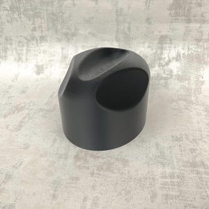 Könnte beinhalten: Eine mattschwarze Sprühkopfkappe aus Kunststoff mit abgerundeter, ergonomischer Form. Die Kappe verfügt über eine vertiefte Oberseite für die Fingerplatzierung und eine kreisförmige seitliche Öffnung für ein Sprühdosenventil.