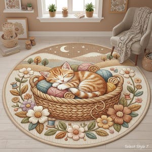Op de afbeelding: Een ronde vloerkleed met een slapende oranje tabby kat in een mand gevuld met garenballen en knopen. Het kleed heeft een landschapsontwerp met een maan en sterren, omringd door bloemen en bladeren.