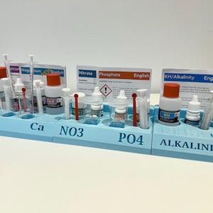 Könnte beinhalten: Ein hellblauer Testkit-Organizer mit mehreren Flaschen, Spritzen und Reagenzgläsern. Die Flaschen haben orangefarbene Kappen. Der Organizer ist mit den Abkürzungen Mg, Ca, NO3, PO4 und Alkalinity beschriftet. Enthält Testanweisungen.